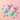 Two stand-up pouches of Wonder Dough Mix candy powder, one filled with light blue powder and the other with mint green powder, arranged on a pastel pink background with matching blue and mint candy swirls and cylinders around them.