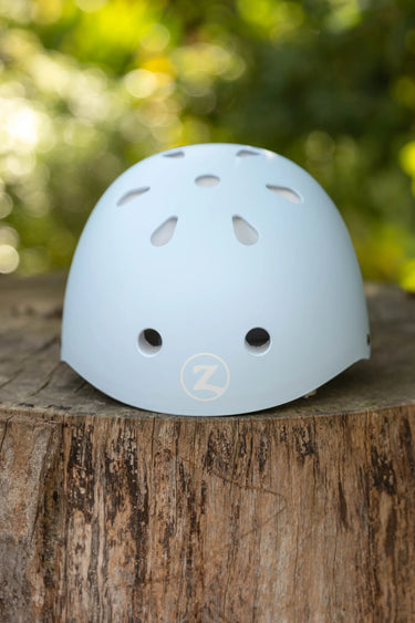 A light blue helmet with ventilation holes, resting on a rustic wooden tree stump with a blurred green outdoor background.