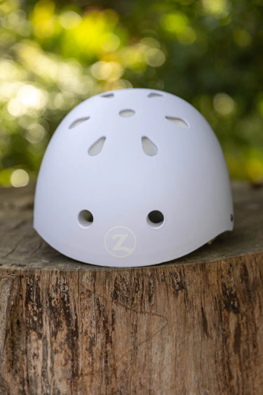 A white safety helmet with ventilation holes and a circular 'Z' logo, resting on a rustic tree stump with a blurred green forest background.