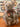 A plush teddy bear with shaggy gray-brown fur, a dark brown bow tie, and cream-colored stitched paws, sitting on a wooden table in a shop setting.