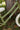 Close-up of a children's balance bike frame in olive green with white snowflake patterns and the brand name 'Zalane' on the down tube, photographed outdoors against a tree trunk and grass.