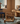 Wicker toy dollhouse with figurines on a carpeted floor in a room with wooden walls and a window.
