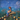 A soft, textured fantasy artwork showing a child-like figure sitting on a mushroom in a blue, dreamy landscape, holding a glowing lantern. The scene includes floating white shapes and warm glowing orbs across the ground.