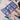 Person holding a blue card with building illustrations and wooden blocks on a textured surface, with 'KAPLA' branding.