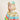 A child wearing a gold glitter and mint green parrot feather headband and a shiny gold cape with colorful fringe in red, green, yellow, and blue, set against a plain beige background.