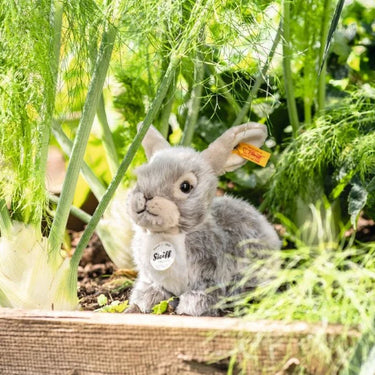 Plush rabbit toy with a Stuffed tag in a garden setting