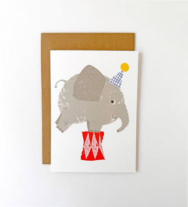 Card with an illustration of an elephant wearing a party hat and standing on red shoes, framed by a brown border.