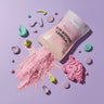 A pink pouch labeled 'WONDER POWDER MIX' lies on a lavender background with spilled pink powder, pastel candy-like pieces, and a pink unicorn-shaped cookie cutter or mold.