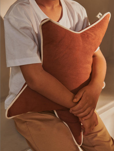 Child holding a brown cushion against a neutral background
