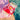 A pink mesh pool bag filled with swim accessories, including a red swim cap and a yellow-and-red swim float, placed beside a swimming pool.