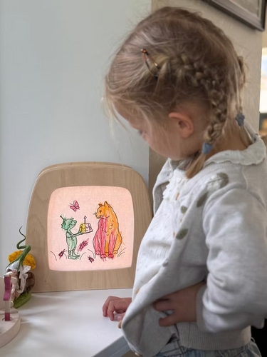A child inf ront a lamp with a picture she has coloured in.