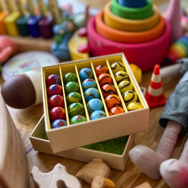 A box of glass marbles in a busy playroom with dolls and wooden toys 