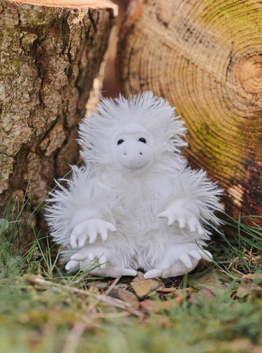 White fluffy creature sitting on the ground with wooden logs in the background