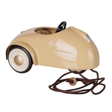 A vintage-style toy car in beige with black wheels, a black steering wheel, and a brown pull cord, shown on a plain white background.