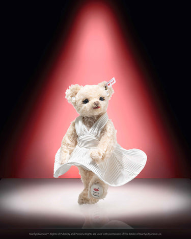 A Steiff collectable teddy bear representing Marilyn Monroe wearing a white dress with a red spotlight background