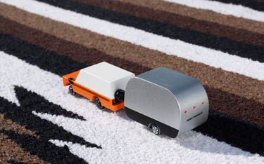 A toy car towing an toy airstream camper  on a striped fabric background