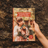 A book called Wild Celebrations being held by a child's hand against a bark background