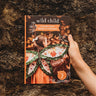 A book called Wild Child being held by a child's hand against a bark background