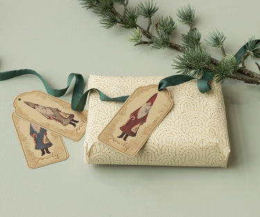 Gift wrapped in textured paper with decorative tags and a green ribbon, set against a light background.