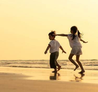 Two children holding hands and running on a beach at sunset.