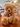 A plush teddy bear with fluffy tan fur with glittery silver accents sits on a wooden table in a shop. The bear wears a matching knit scarf and has a product tag attached to its neck. He is labelled bear A.