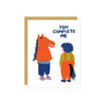 A white greeting card with a gold envelope behind it, featuring a humorous illustration of an orange horse-like figure and a person in orange overalls with the text 'YOU COMPLETE ME'.