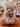 A plush teddy bear with light gray and sparkling fur sits on a wooden table in a gift shop. The bear has a dark gray winter scarf and a red hangtag attached to its neck. He is labelled Bear B.