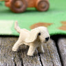 Small felt dog figurine on a wooden surface with a toy truck in the background.