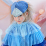 Child wearing a blue dress with ruffled layers and a matching hat with glittery band.