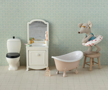 Miniature bathroom set with bathtub, toilet, and vanity against a patterned wall.