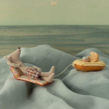 Stuffed dad mouse  lying on a floral mat with a small boat, all on a textured green surface.