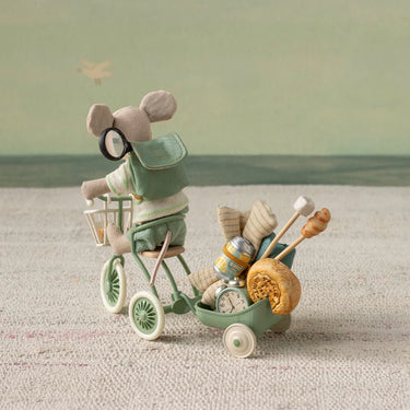 Toy mouse on a bicycle with a cart full of items against a plain background