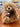 A fluffy beige teddy bear plush toy with a dark brown sheer bow and a product tag, sitting on a wooden table in a store setting with the letter A on its tag.