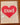 A square greeting card with a large red heart and the word 'Dad' in white, photographed on a wooden surface inside a clear protective sleeve.