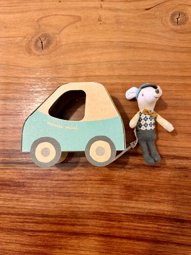 A cardboard toy car in mint green and beige with a small plush maileg mice doll dressed as a driver, placed on a warm brown wooden tabletop.
