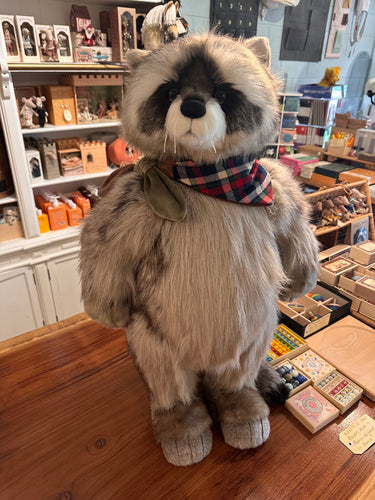 Stuffed raccoon toy with a plaid bow tie on a wooden surface