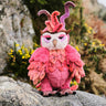 Pink owl plush toy with a unique design on a rock with natural background