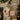 A Christmas stocking with a beige body, gray velvet trim, and an embroidered reindeer pulling a sleigh hangs on a fireplace mantel beside wrapped gifts and a decorated Christmas tree.
