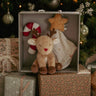 Plush reindeer toy with candy cane and star in a box, surrounded by Christmas decorations.