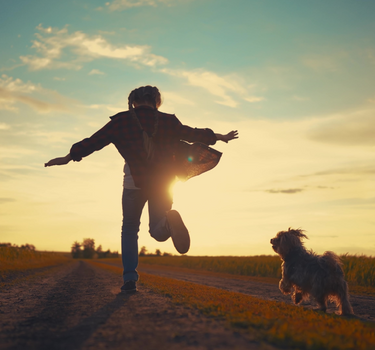 Person and dog running on a dirt path with a sunset in the background