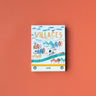A boxed stamp set titled "VILLAGES" with illustrated houses, trees, clouds, and a bicycle on the front, photographed on a solid coral-orange background. The brand name "londii" is visible near the bottom.
