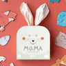 A puzzle called MaMa in a beige box with cloth bunny ears on a red background 