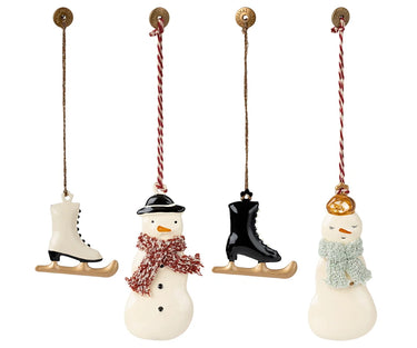Four Christmas hanging ornaments shaped like winter motifs: a white ice skate, a snowman with a black hat and red patterned scarf, a black ice skate, and a snowman with a gold hat and light blue scarf. Each ornament hangs from a red-and-white striped string with a gold loop at the top, shown on a plain white background.
