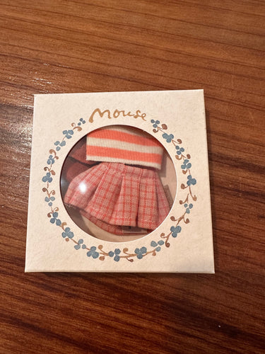A miniature doll clothing set inside its original packaging, featuring a red and white plaid skirt and a red and white striped top, displayed on a wooden surface.