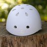 A white safety helmet with ventilation holes and a circular 'Z' logo, resting on a rustic tree stump with a blurred green forest background.