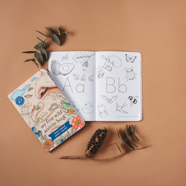 A book with a traceable letters and pictures to colour in surrounded by leaves on a beige background