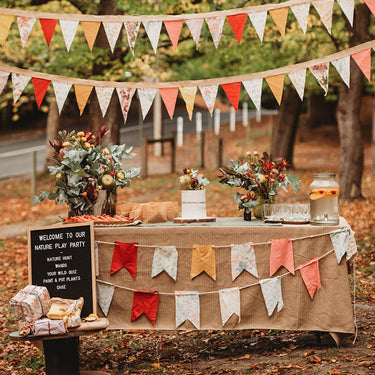 A party table set up in the forest with bunting, flowers, presents and a sign