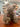 A fluffy brown teddy bear with a brown bow tie sits on a wooden table in a shop setting.