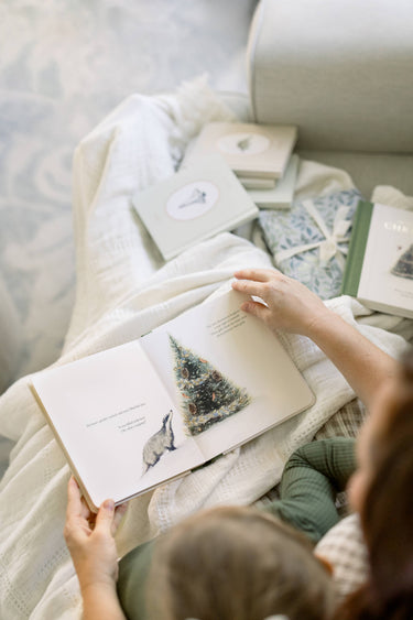 Person reading a book with a Christmas tree illustration on a cozy blanket