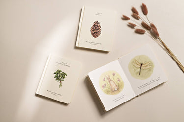 Three books with botanical illustrations on a beige surface and some wild flowers